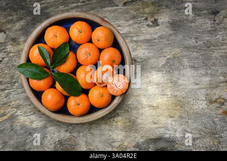 Un bol rempli d'oranges de mandarine clémentine fraîches mûres sur un dessus de table en ardoise, avec espace de copie. Banque D'Images