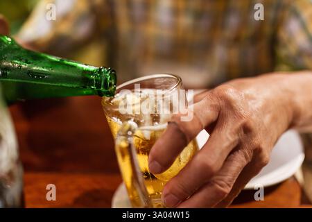 La main verse une boisson alcoolisée rafraîchissante de la bouteille verte dans un verre pendant le dîner Banque D'Images