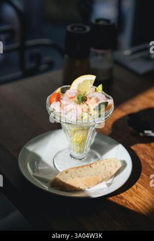 Apéritif cocktail de crevettes avec légumes servi avec du pain brun dans un verre sur une table en bois dans le restaurant Banque D'Images