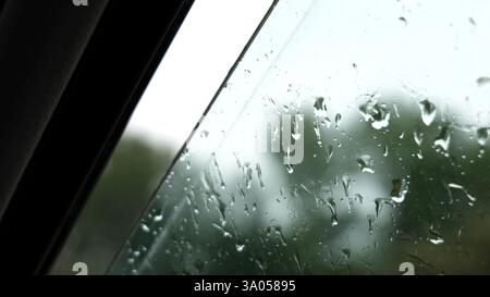 Pluie tombant sur la fenêtre de voiture ouverte humide, gros plan des gouttes de pluie sur le verre du véhicule, intérieur de la voiture pendant la pluie, plan détaillé de l'eau de pluie sur la fenêtre, orageux nous Banque D'Images