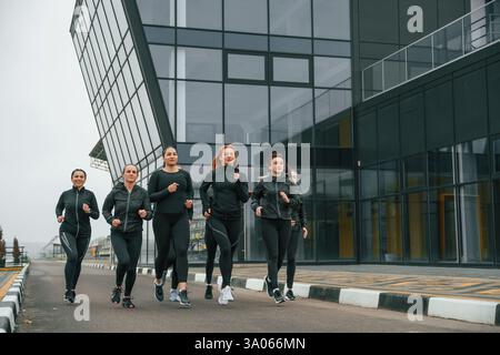 Courir ensemble. Groupe de femmes sportives est à l'extérieur près du bâtiment noir. Banque D'Images