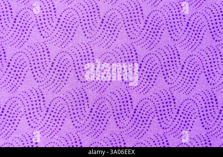 Gros plan au-dessus de la vue de vagues de points bleus en cascade sur un tissu violet clair étalé à plat sur un fond blanc. Banque D'Images