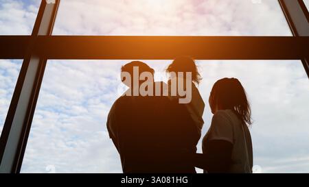 Famille regardant par la fenêtre de l'aéroport au ciel nuageux Banque D'Images