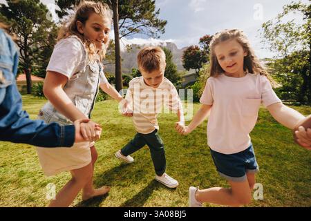 Un groupe d'enfants heureux se tenant la main et jouant un jour ensoleillé dans un parc, profitant d'activités de plein air et mettant en valeur l'amitié, la joie et ensemble Banque D'Images