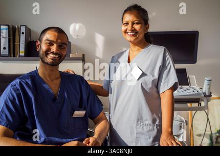 Portrait d'une travailleuse de santé souriante portant des gommages médicaux debout près d'un collègue masculin à la clinique Banque D'Images