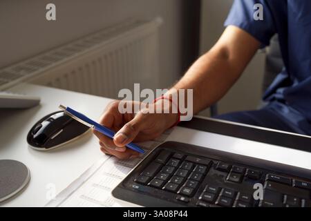 Travailleur de santé masculin tenant un stylo près du clavier au bureau à l'hôpital Banque D'Images