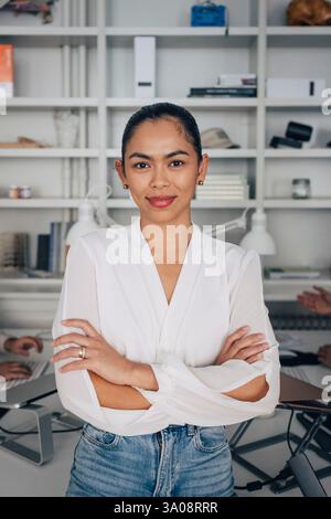 Portrait de femme souriante professionnelle créative debout avec les bras croisés dans le bureau Banque D'Images