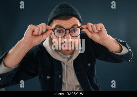 Mec drôle jouant avec des lunettes. Bel homme est dans le studio sur fond bleu. Banque D'Images