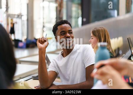 Souriant jeune étudiant masculin regardant en arrière tout en étant assis par une amie dans la classe à l'université Banque D'Images