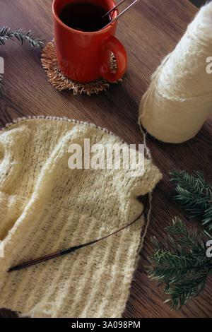 Motif de tricot jaune avec branche de conifère et thé dans une tasse orange. Mode tricoté. Crochet à tricoter en coton avec aiguilles à tricoter et tasse à thé Banque D'Images