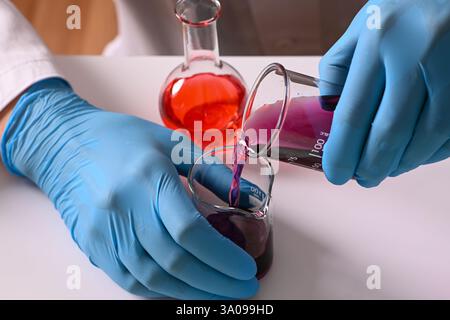 Gros plan de mains de scientifiques mélangeant des liquides chimiques dans des béchers de laboratoire pour la recherche pharmaceutique. Banque D'Images