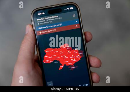 Image illustrative d'une personne tenant un smartphone à la main affichant une carte de l'Ukraine, marquant en rouge les régions sous la menace russe, alors que des sirènes de raid aérien sonnent à travers Kiev. Une alerte MiG-31K a été déclarée dans toute l'Ukraine au moment de la prise de la photo. Banque D'Images