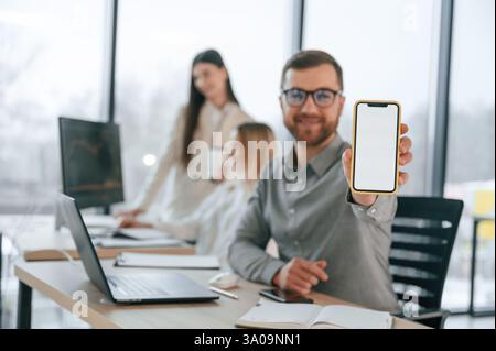 Sourire et tenir le smartphone. Une équipe performante travaille ensemble au bureau. Conception de l'entreprise. Banque D'Images