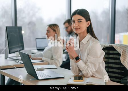 La femme est assise près d'une table avec un ordinateur portable. Une équipe performante travaille ensemble au bureau. Conception de l'entreprise. Banque D'Images