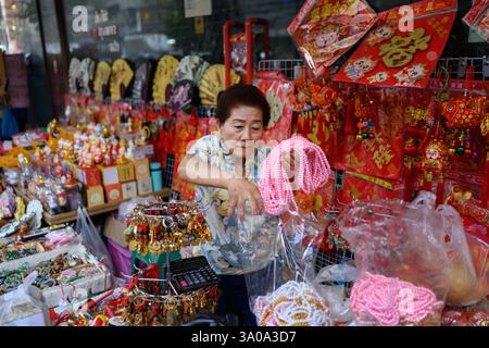 Bangkok, Thaïlande. 18 février 2025. Une femme vendant des souvenirs chinois et des cadeaux d'un étal côté rue le long de Yaowarat Road, Chinatown, Bangkok, T. Banque D'Images
