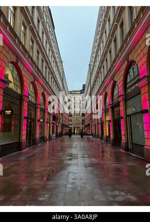 « Une galerie marchande magnifiquement éclairée à Helsinki, en Finlande, à l'architecture symétrique et à l'éclairage rose reflétant le sol mouillé. Banque D'Images