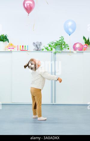Jolie fille de 3 ans avec le syndrome de Down célébrant son anniversaire dans une salle de jeux décorée de ballons. Fête d'anniversaire pour enfants. Banque D'Images