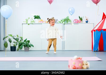 Jolie fille de 3 ans avec le syndrome de Down célébrant son anniversaire dans une salle de jeux décorée de ballons. Fête d'anniversaire pour enfants. Banque D'Images
