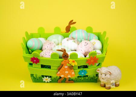 Oeufs de Pâques colorés dans un panier vert sur fond jaune. Fête de Pâques. Photo de haute qualité Banque D'Images