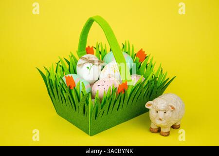 Panier vert avec des oeufs colorés de Pâques et des moutons sur un fond jaune. Photo de haute qualité Banque D'Images