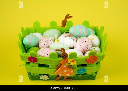 Oeufs de Pâques colorés dans un panier vert sur fond jaune. Fête de Pâques. Photo de haute qualité Banque D'Images