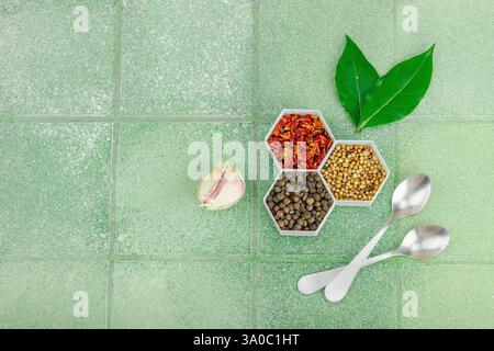 Fond culinaire créatif. Ensemble d'épices parfumées, d'herbes fraîches et de gousses d'ail. Concept d'alimentation saine, cuillères à mesurer. Carreau vert clair, plat Banque D'Images