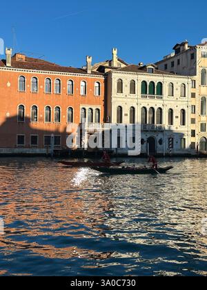 Balade en gondole à travers le Grand canal de Venise au coucher du soleil, avec des bâtiments historiques bordant l'eau et une vue panoramique sur le pont du Rialto. Banque D'Images