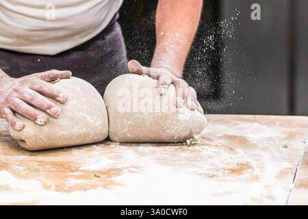 Un boulanger pétrit la pâte à pain dans la boulangerie. Banque D'Images