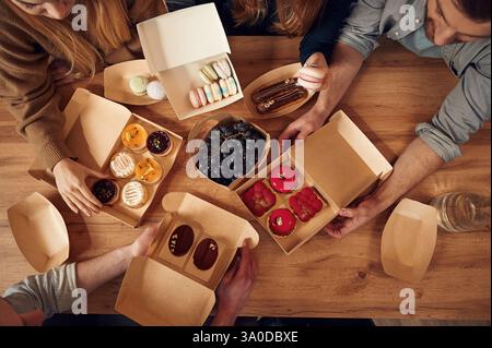 Vue de dessus de la table avec de la nourriture dessus, les mains des gens qui la prennent, mangent. Macarons, myrtilles, desserts, repas pâtissier. Banque D'Images