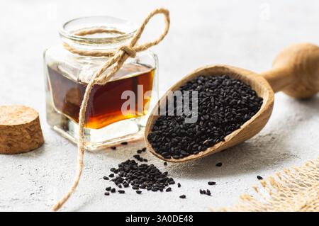 Bouteille en verre d'huile essentielle de graines de cumin noir, Nigella Sativa en cuillère sur fond rustique. Phytothérapie organique pour de nombreuses maladies, cumin noir Banque D'Images