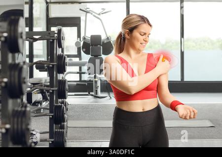 Jeune femme avec douleur dans l'exercice d'épaule avec un haltère dans un gymnase Banque D'Images