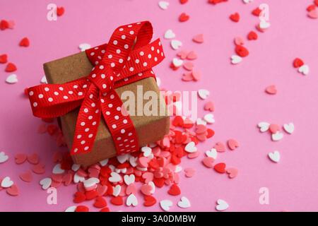 Boîte cadeau avec noeud en ruban rouge avec des points blancs entourés de coeurs colorés Banque D'Images
