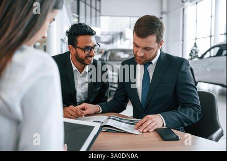 Choisir l'automobile. Trois personnes travaillent ensemble dans le showroom automobile. Banque D'Images