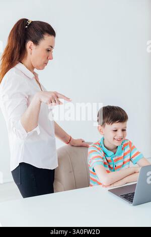 Une enseignante aide un garçon sur ordinateur portable à jouer en ligne à l'école Banque D'Images