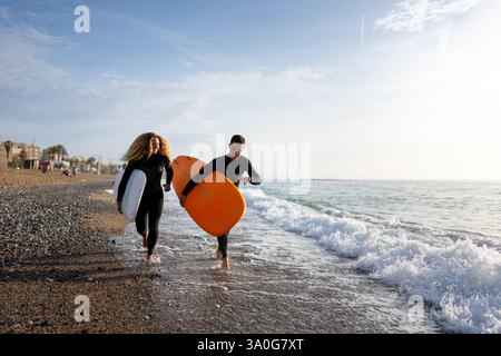 Beau couple de surfeurs heureux s'amuser sur la plage, courir avec planche de surf aux vagues Banque D'Images