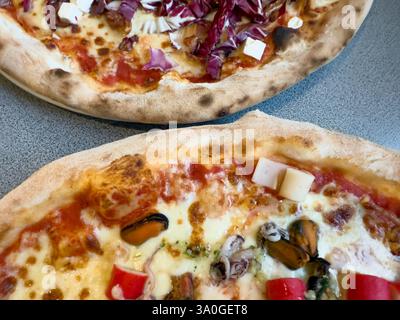 Vue de haut en bas de deux pizzas artisanales : l'une garnie de fruits de mer, de bâtonnets de crabe et de fromage ; l'autre avec du radicchio et du fromage feta. Banque D'Images