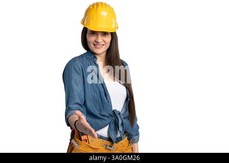 Une travailleuse de la construction souriante portant une chemise en Jean et un casque jaune tend la main pour une poignée de main. Cette image représente le professionnalisme Banque D'Images