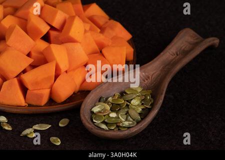 Nourriture saine. Au centre de la composition se trouve une cuillère en argile avec des graines de citrouille. Des morceaux de citrouille orange vif reposent sur une assiette à proximité. Banque D'Images