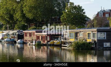 Péniches avec panneaux solaires sur le toit du bateau de la maison un jour gris avec un soleil bas reflétant dans l'eau. Banque D'Images
