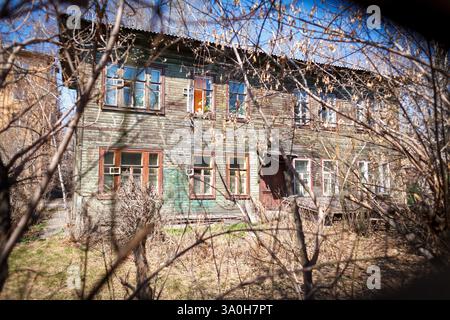 Une vieille maison en bois de deux étages altérée entourée de branches sèches et de buissons par une journée ensoleillée Banque D'Images