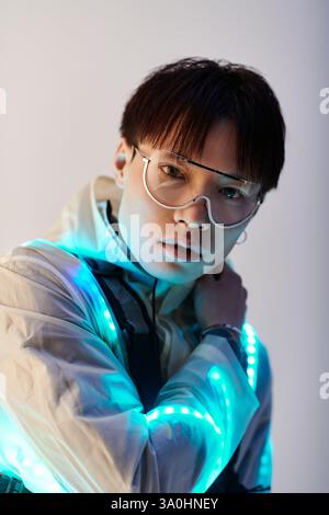 Un jeune homme asiatique à la mode pose avec des accessoires lumineux, affichant un look assuré. Banque D'Images