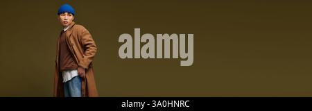Un jeune et beau homme asiatique vêtu d'un manteau tendance et d'un bonnet bleu respire le style et la confiance. Banque D'Images