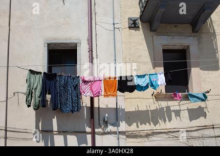 Vêtements colorés séchant sur une ligne attachée à une façade de bâtiment rustique à Naples, en Italie, représentant la pauvreté urbaine Banque D'Images