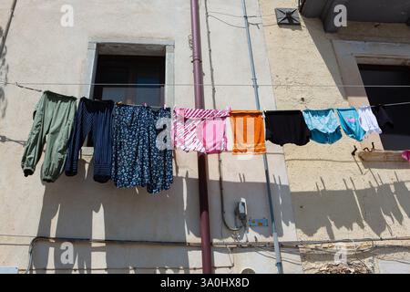 Vêtements colorés séchant sur une ligne attachée à une façade de bâtiment rustique à Naples, en Italie, représentant la pauvreté urbaine Banque D'Images