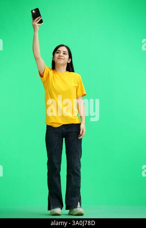 Une femme, pleine longueur, sur fond vert, agitant son téléphone Banque D'Images