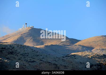 Une vue panoramique d'une montagne de radars militaires entourés d'herbe sèche et d'arbres clairsemés à la lumière du soleil. Le ciel bleu met en valeur la sérénité et l'être naturel Banque D'Images