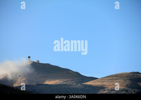 Une vue panoramique d'une montagne de radars militaires entourés d'herbe sèche et d'arbres clairsemés à la lumière du soleil. Le ciel bleu met en valeur la sérénité et l'être naturel Banque D'Images