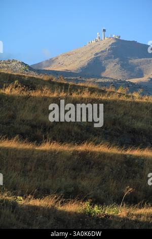 Une vue panoramique d'une montagne de radars militaires entourés d'herbe sèche et d'arbres clairsemés à la lumière du soleil. Le ciel bleu met en valeur la sérénité et l'être naturel Banque D'Images