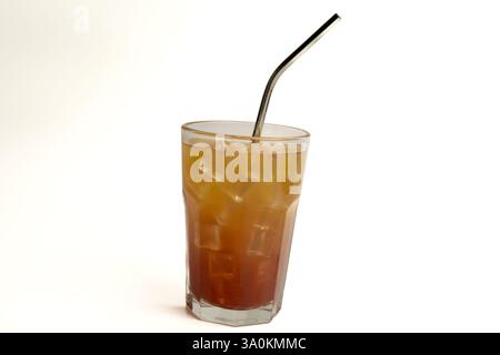 Gros plan d'un grand verre rempli d'une boisson fraîche d'été sur un fond blanc. La boisson est de couleur ambre, avec de la glace et une paille métallique. Studio shot e Banque D'Images
