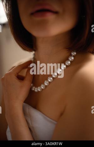 Une jeune femme regarde doucement, portant une élégante boucle d'oreille en perles et un collier assorti. Banque D'Images
